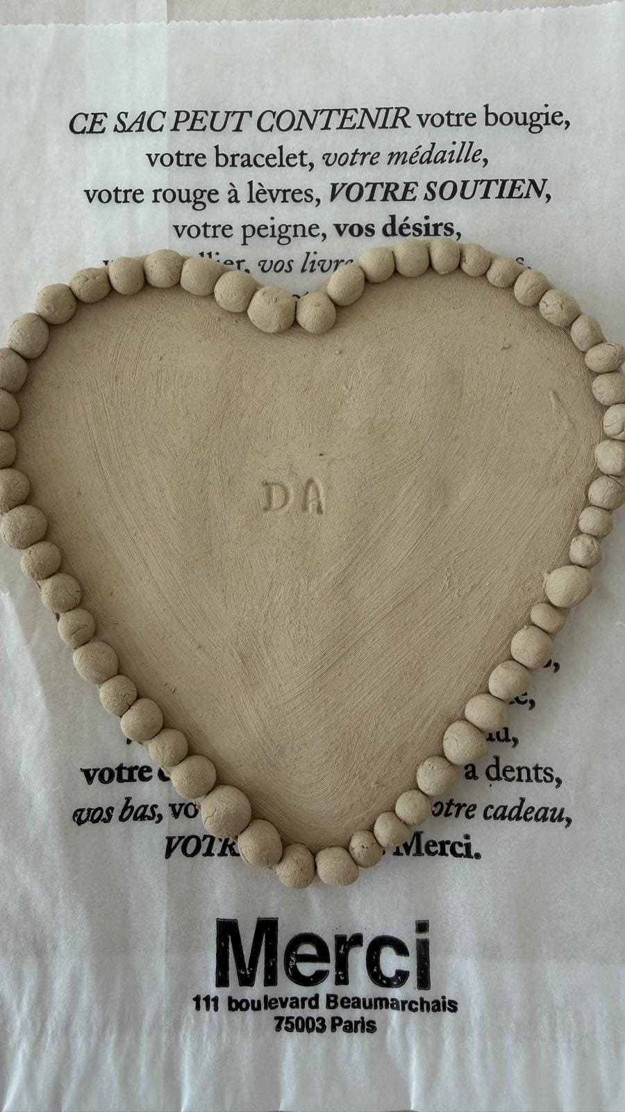 A hand-built heart-shaped clay dish with a rolled bead edge and stamped initials