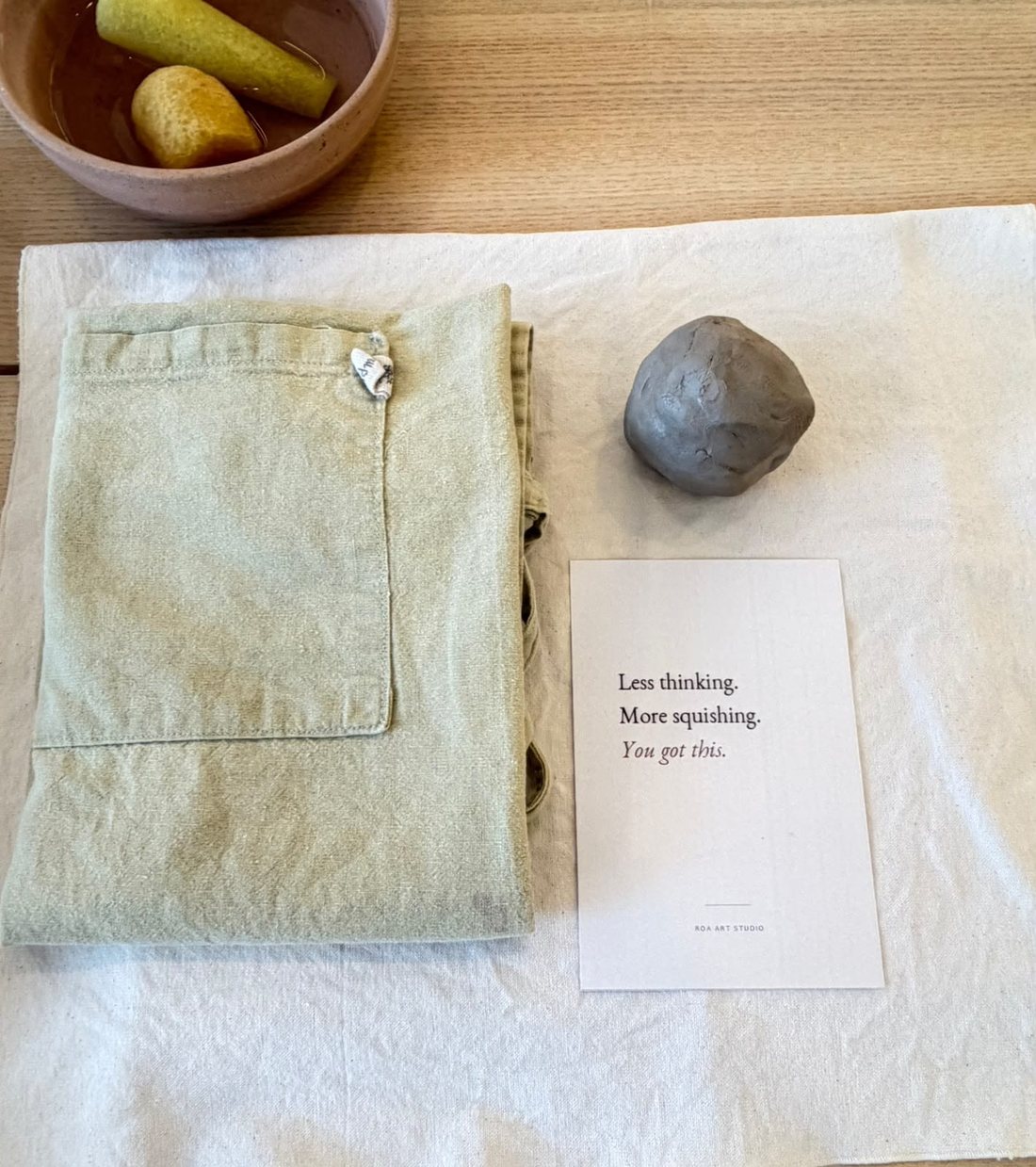 An apron, a ball of clay and a ROA Art card reading Less thinking, more squishing, you got this